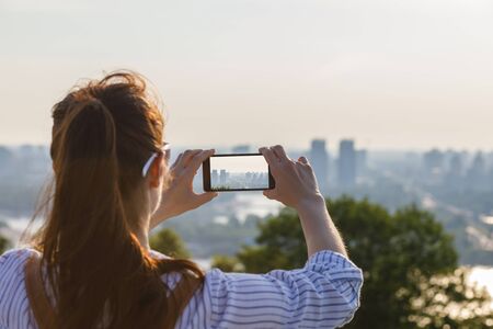 A woman photographs the urban landscape on a phone.の写真素材