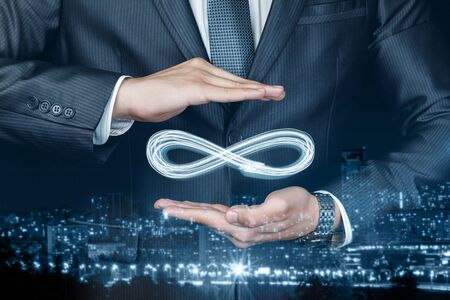 Concept of unlimited Internet. Businessman shows sign of infinity on the background of the city. The concept of unlimited Internet.の写真素材