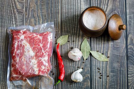 The meat is packed in a vacuum with spices and pepper and a nitrite salt on wooden background.の写真素材