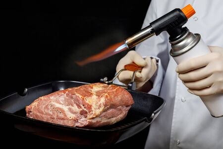 Cooking meat with the help of a gas burner on a dark background.の写真素材