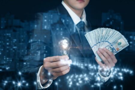 The concept of financial ideas. Businessman with dollar notes and a burning lamp on the background of the city.の写真素材