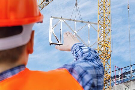 A construction engineer supervises the construction crane on sky background.