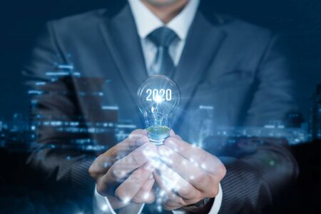 The concept of a new idea in 2020. Businessman holding a light bulb with glowing numerals 2020 and...