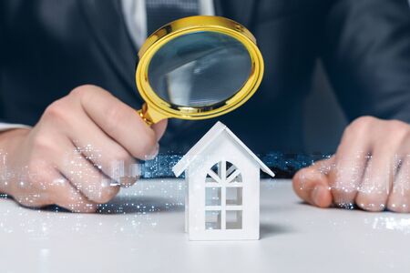 The concept of the study and inspection of the property. Looking through a magnifying glass at a model home.の写真素材