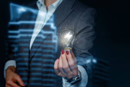 The concept of a spark of an idea in business. Businesswoman showing light bulb burning on blurred background.の写真素材