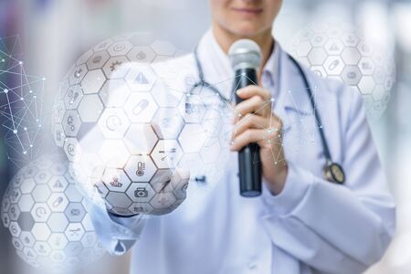 The doctor stands with a microphone and clicks on the medical icons on a blurred background.