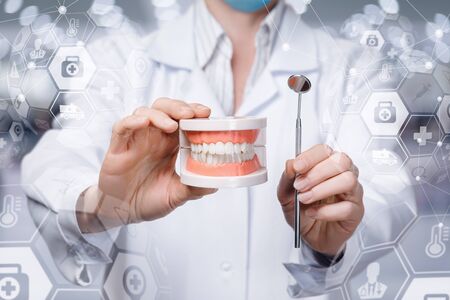 The concept of dental treatment. Doctor shows jaw with teeth and a tool on a blurred background.の写真素材