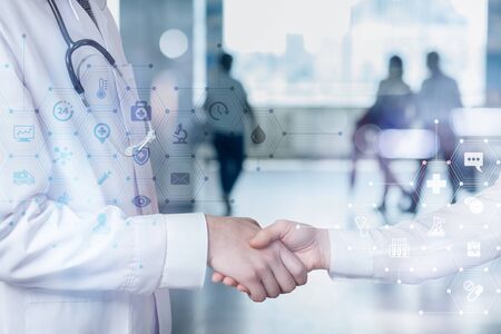 The doctor shakes hands with the patient on a blurred background.
