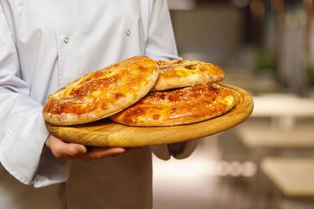 The cook shows a pitas on a wooden board on a blurred background.
