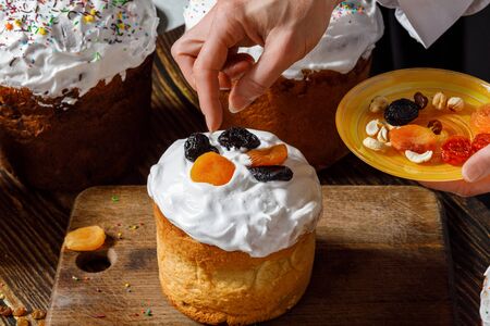 Cook decorates Easter cake with dried fruits on a dark background.