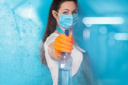 A cleaning lady in a mask disinfects a blue background.