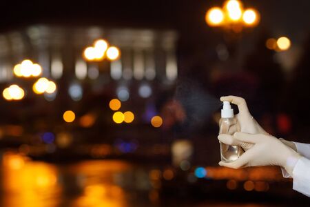 The concept of disinfection and control of coronavirus. Hands with a disinfectant spray against the background of the night city.の写真素材