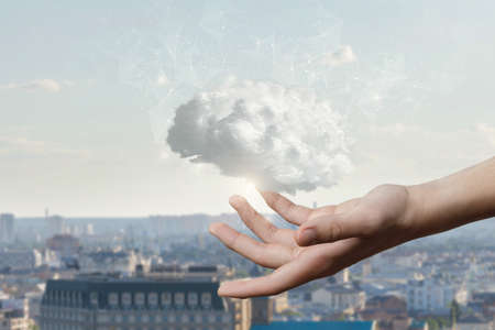 The hand shows a brain consisting of clouds on the background of the city.