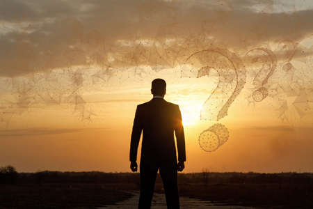 The businessman looks into the distance at the questions that have appeared from the network against the background of a sunny sunset.の写真素材