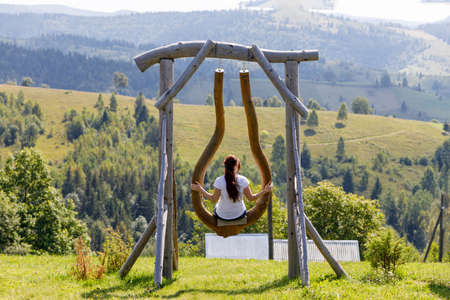 A woman rides on a swing against the backdrop of a mountainous area.