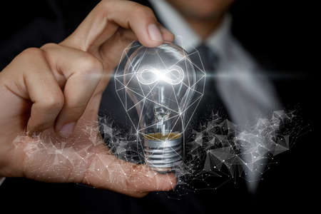 Endless business ideas concept. The hand shows a light bulb with a burning hologram of infinitie inside.の写真素材
