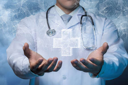The concept of providing health care. Doctor shows a hologram of the Cross on a blurred background.の写真素材