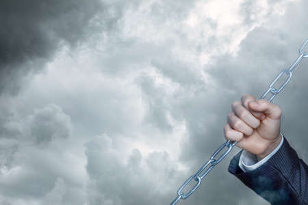 The hand of a businessman holds a chain against the background of the sky.の写真素材