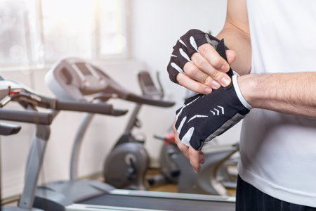 Athlete wears fitness gloves on the background of treadmills.