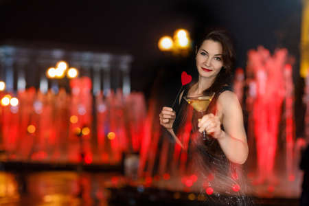 Valentines day celebration concept. Woman with valentine card and glass of martini stands on blurred...