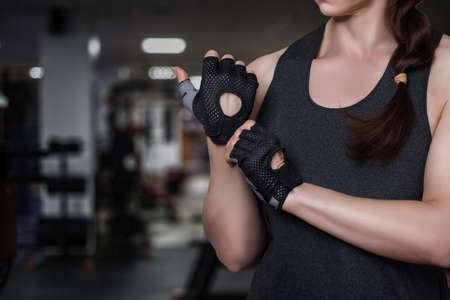 Woman puts on fitness gloves on the background of the gym.