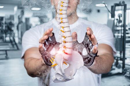 Young athlete protects the spine with a hand gesture on the background of the gym.の写真素材