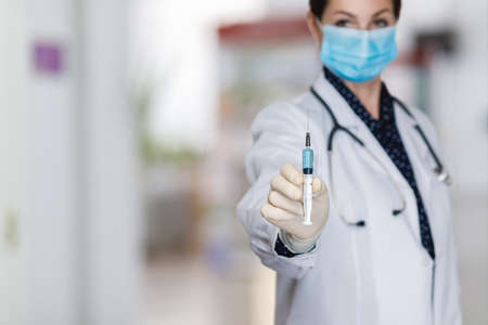 Female doctor shows syringe with vaccine on blurred background.