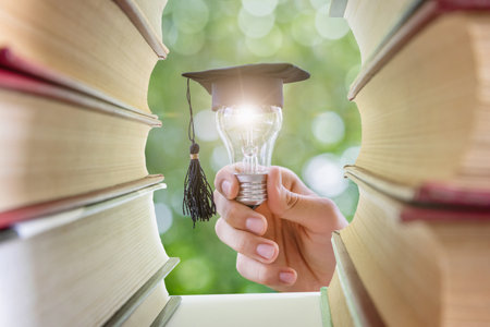 Learning and education concept. A light bulb with an academic cap in hand in front of textbooks.の写真素材