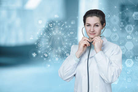 Doctor stands holding stethoscope on blurred background.の写真素材