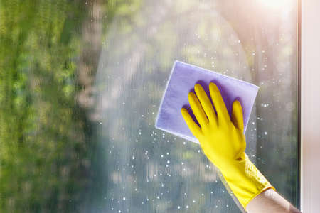 The cleaning woman hand wipes the window from the cleaning agent with a rag.