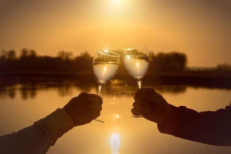 Couple clink glasses against the background of a sunny sunset near the river.の写真素材