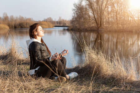 Woman recovers strength meditating on the background of the river in spring.の写真素材
