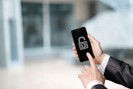 The concept of removing protection from a mobile device. The hand shows a mobile phone with an open padlock on a blurred background.の写真素材