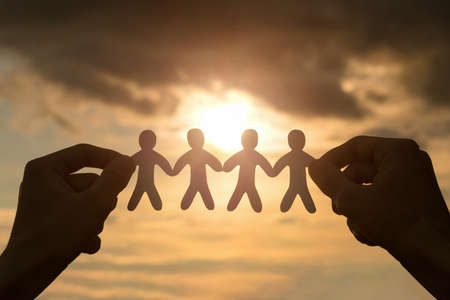 Hands hold a group of paper cut people on the background of the sun.