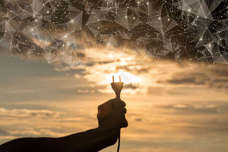 Hand holds out an electric plug to the sun against the sky.
