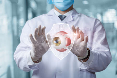 Doctor shows a model of the eye protected by a shield on a blurred background.の写真素材