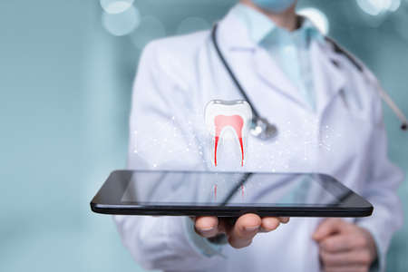 Doctor dentist shows a model of a tooth on a tablet on a blurred background.の写真素材