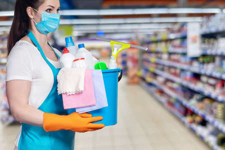 Cleaning lady with cleaning products in a bucket stands on a blurred background.の写真素材