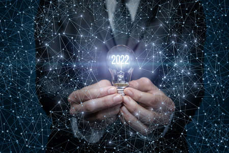 Concept new year new ideas in 2022. Light bulb with glowing numbers 2022 on a blue background...