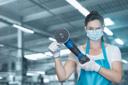Service concept grinding and cutting. Woman worker in a smear holds a grinder on a blurred...