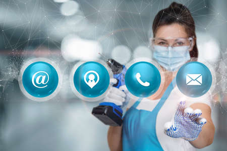 A worker woman with a drill in her hands clicks on the contact icons of the service.の写真素材