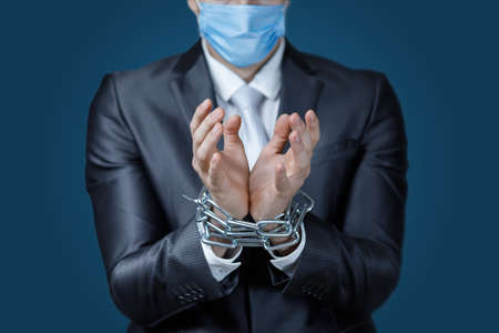Concepts of business restrictions during a pandemic. Businessman in a mask with his hands tied in...