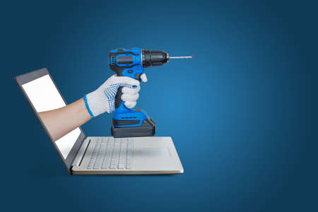 Hand with dril emerging from laptop screen on blue background.の写真素材