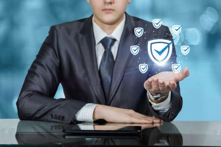 Business man sitting at the table shows quality assurance icons.
