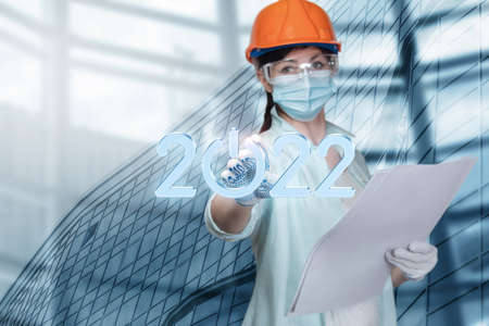 Construction worker clicks on new year 2022 on blurred city background.