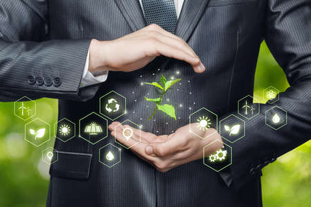 Environmental protection concept. Businessman protective gesture protects sprout on blurred background.の写真素材