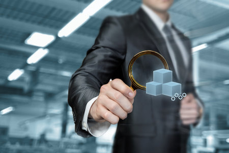 Businessman looking at box through a magnifying glass on blurred production background.の写真素材