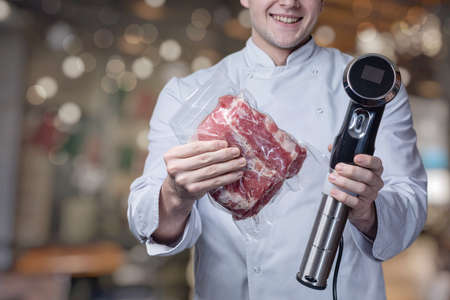 A cook wrapped in a vacuum with meat and a device for cooking with a low temperature on a blurred background.の写真素材