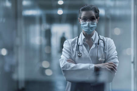 Medical worker in protective mask stands against a dark background.