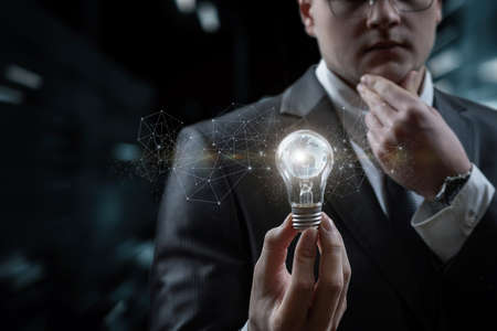 Businessman thinks looking at a burning light bulb with a globe inside on a blurred background.の写真素材